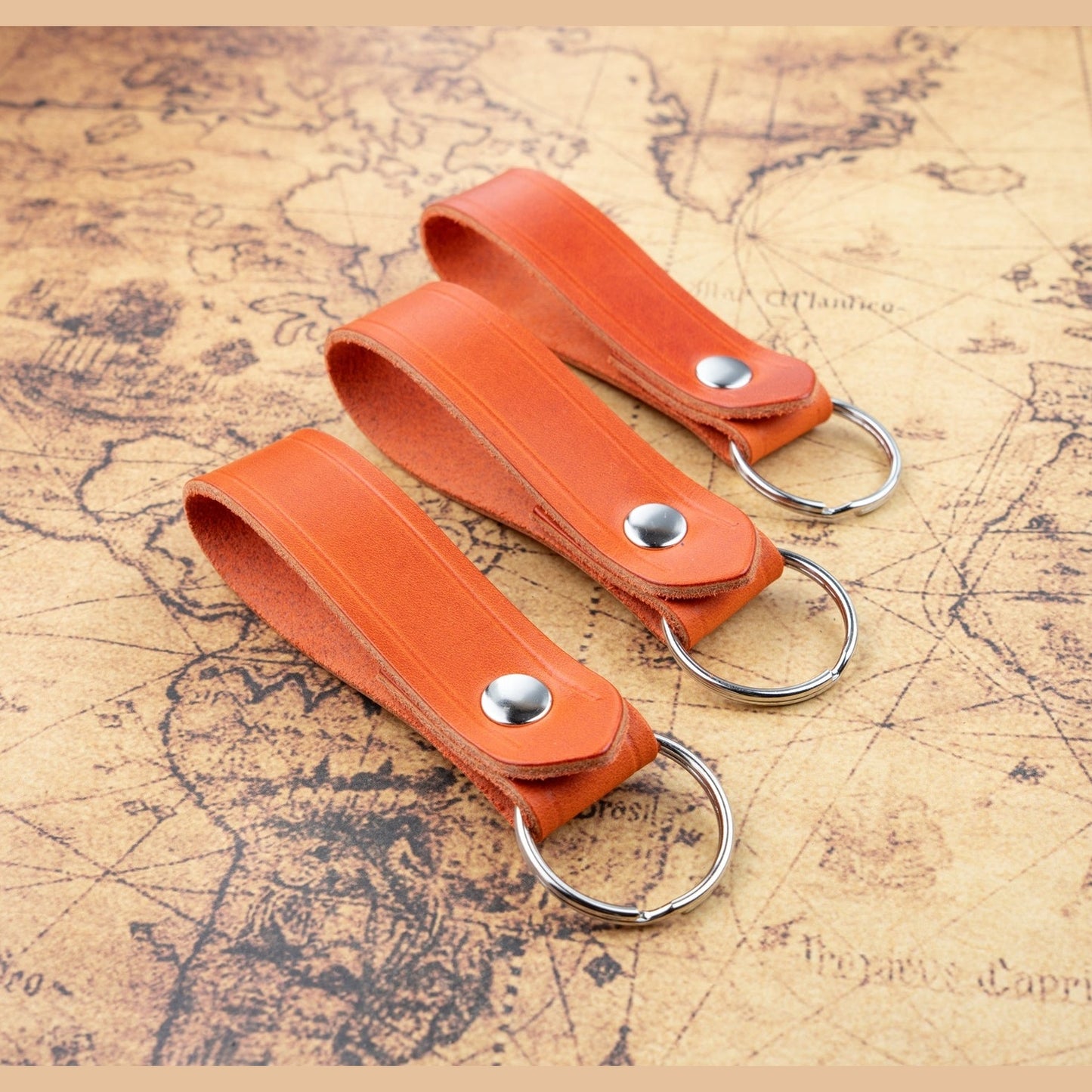 Two orange leather keychains with metal rings on a vintage map background